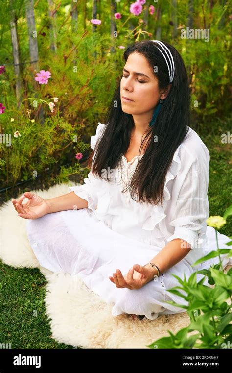 Middle Age Woman Meditating In Green Garden Sitting On Sheep Skin