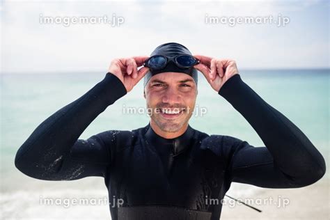 Young man in wetsuit and swimming goggles standing on beachの写真素材