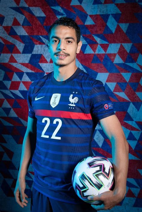 A Man Holding A Soccer Ball In Front Of A Blue And Red Wall With Triangles