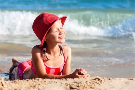 Menina Crian A Feliz Em Vermelho Deitado Na Praia Ensolarada No Fundo