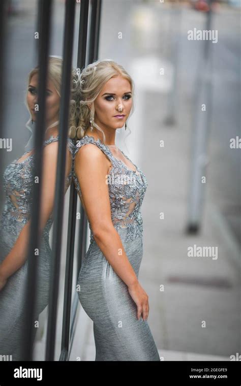 Attractive Blonde Lady Wearing A Long Silver Dress Is Posing Leaning