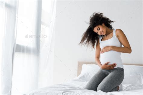 Happy Pregnant African American Woman Touching Belly While Sitting On