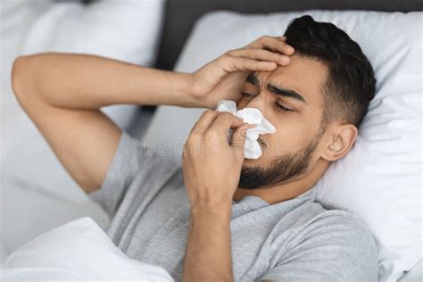 Seasonal Flu Sick Arab Man Blowing Runny Nose While Lying In Bed Stock