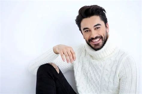 A Man Sitting On The Floor Wearing A White Sweater And Black Pants