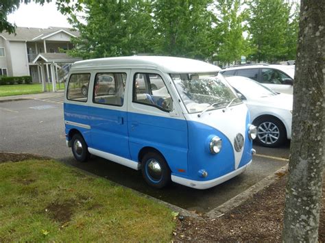 An Old Blue And White Van Parked In A Parking Lot Next To Another Car