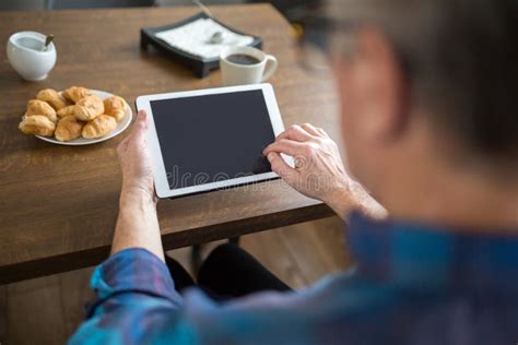 Homem Superior Que Guarda A Tabuleta Na Mesa De Cozinha Foto De Stock