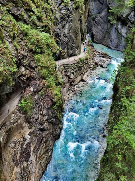 A Person Standing On The Edge Of A Cliff Next To A River With Blue Water