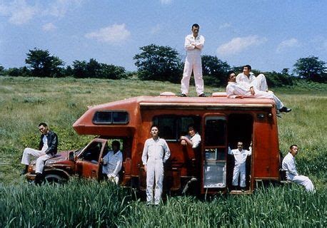 Men Standing On Top Of An Old Van In The Middle Of A Grassy Field With