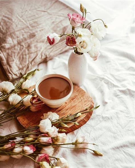 A Cup Of Coffee And Some Flowers On A Wooden Tray Next To A Bed With