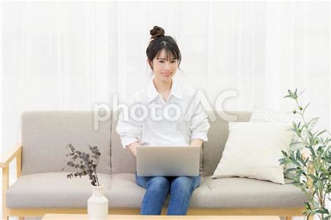 部屋のソファーに座ってノートパソコンを操作する若い女性 No 4641690｜写真素材なら「写真ac」無料（フリー）ダウンロードok