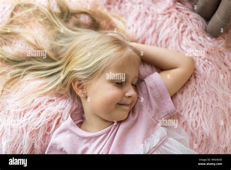 Cute Little Girl With Long Blonde Hair Lying On Pink Fur Blanket With