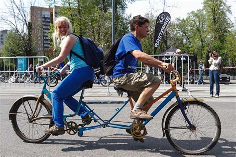 A Man And Woman Riding A Bike Down The Street