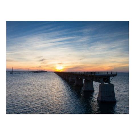 the sun is setting behind a bridge over water