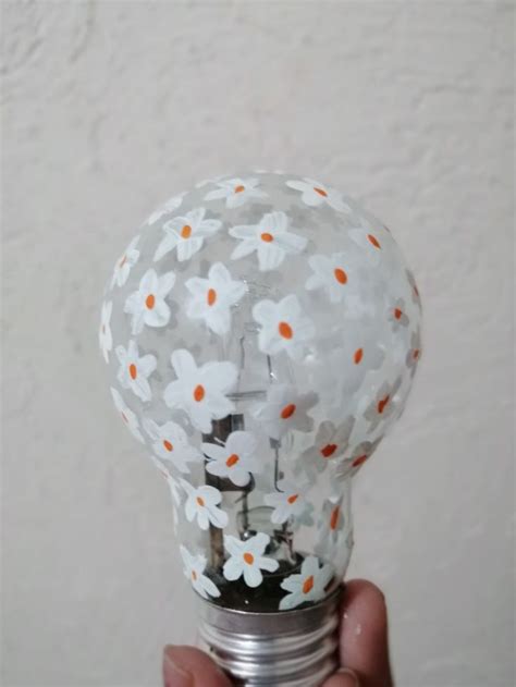 A Light Bulb Decorated With White And Orange Daisies Is Being Held By A