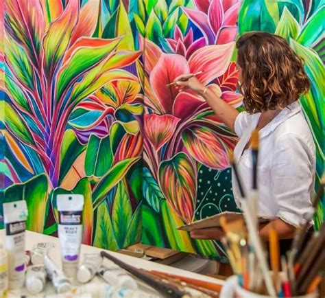 a woman in white shirt painting flowers on wall next to easel with ...