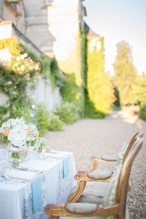 The Table Is Set For Two Outside On The Graveled Path With Flowers In Vases