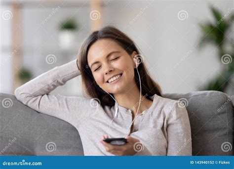 Woman Wearing Earphones Sitting On Couch Holding Phone Listening Music