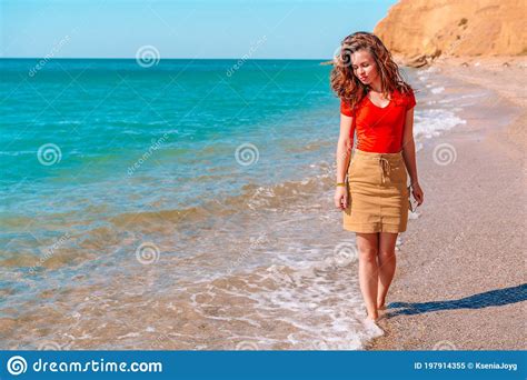 Charming Brunette Woman Walks Along The Beach And Admires The Azure