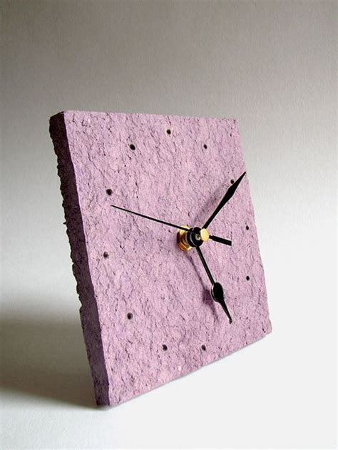 A Clock Made Out Of Concrete On A White Surface With Black Hands And