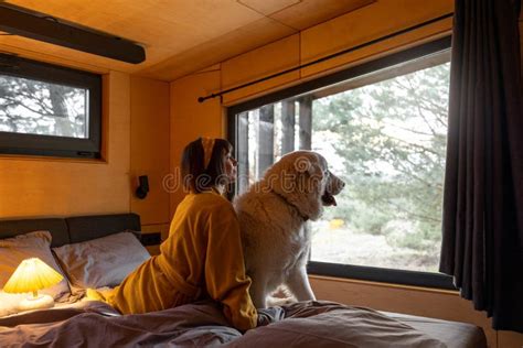 Woman With A Dog Lying On Bed At Wooden Cabin On Nature Stock Photo