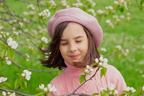 Una niña feliz se para con los ojos cerrados en un manzano blanco