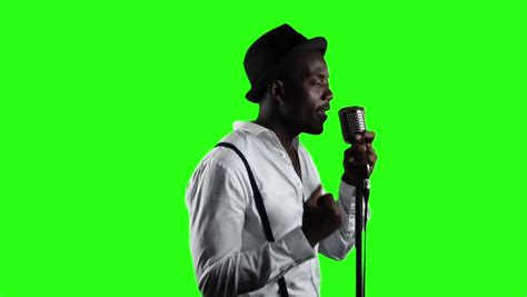 A Vocalist Singing With A Black Microphonewith A Green Screen