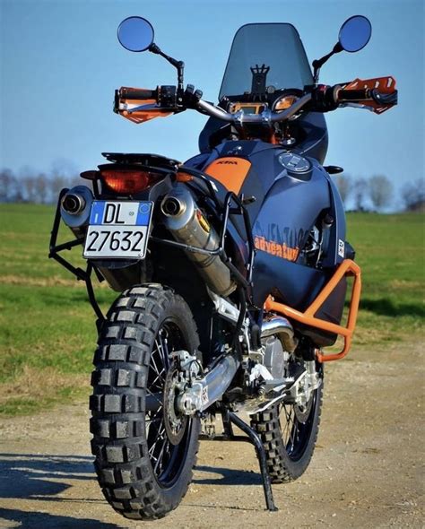 An Orange And Blue Motorcycle Parked On Top Of A Dirt Road Next To A Field