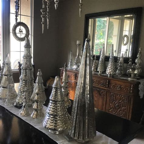 There Are Many Silver Christmas Trees On The Table In Front Of A Mirror