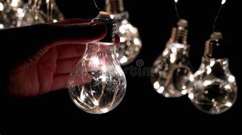 Hand Holds A Light Bulb On The Background Of A Garland Of Glowing Light