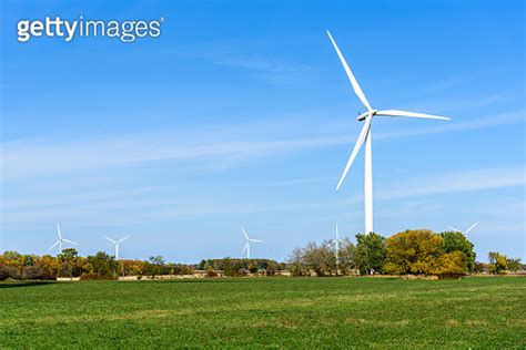 Tall Wind Turbine At The Far End Of A Grassy Field Under Blue Sky In