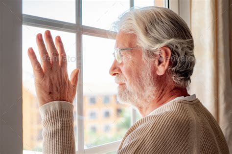 Sad Melancholy Senior Bearded Man At Home Looking Out The Window