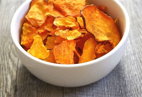 A White Bowl Filled With Orange Chips On Top Of A Wooden Table