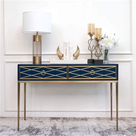 a blue and gold console table with two vases on it, next to a lamp