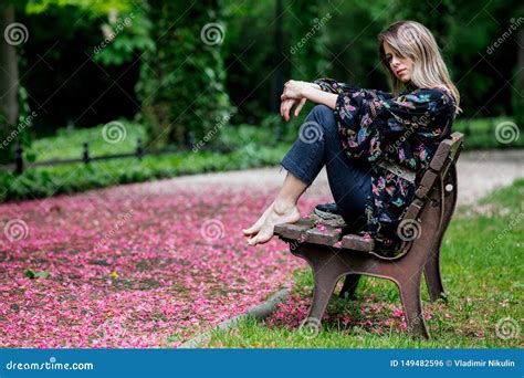 Barefoot Woman Is Sitting On A Bench At Alley With Blossom Trees Stock