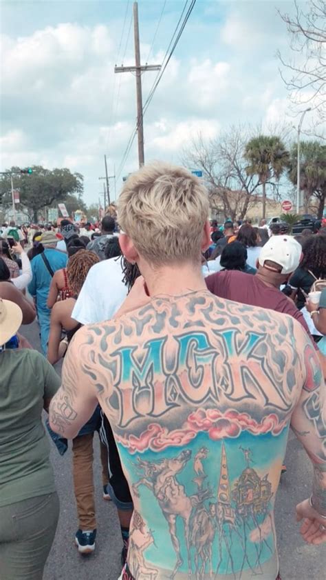 A Man With Tattoos On His Back Walking Down The Street In Front Of A Crowd