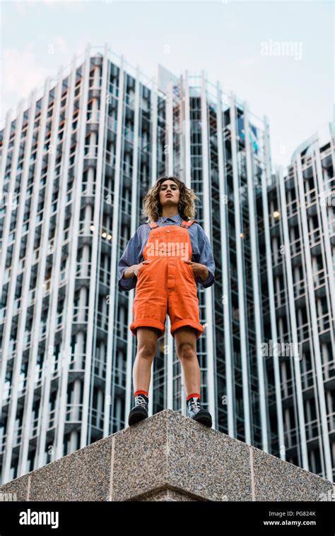 Beautiful Woman Wearing Dungarees Standing On Ledge In Front Of Modern