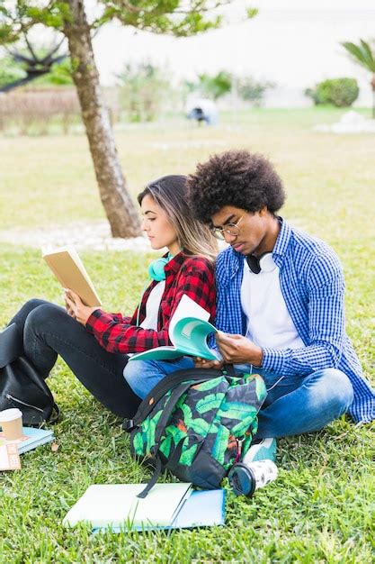 Multi ethnique jeune couple étudiants assis sur le campus en lisant les