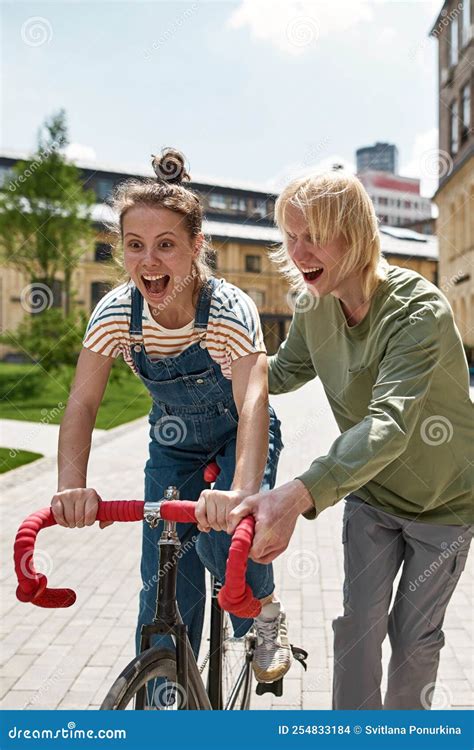 Un Chico Rubio Ayuda A Una Chica Feliz Montando Una Bicicleta En La