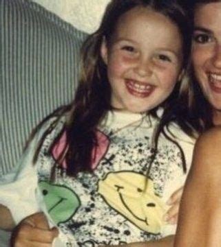 Two Girls Sitting On A Couch Smiling For The Camera With Their Arms