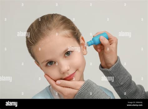 Mother Dripping Medication Into Daughters Ear On Light Grey Background