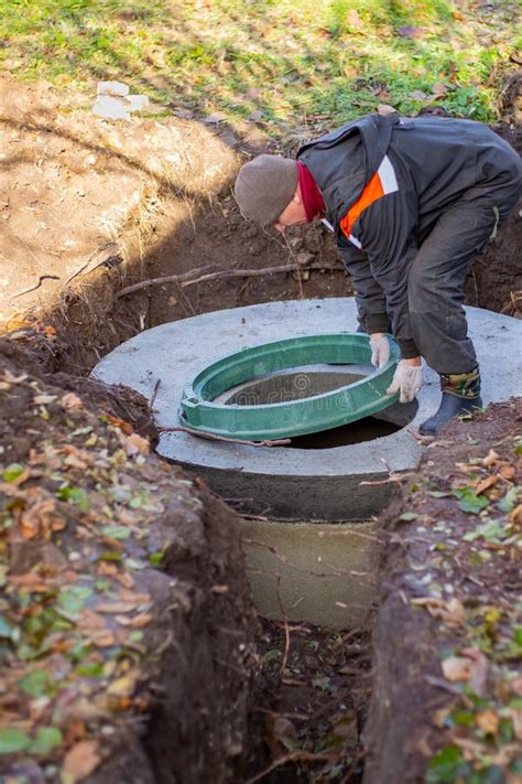 A Worker Installs A Sewer Manhole On A Septic Tank Made Of Concrete