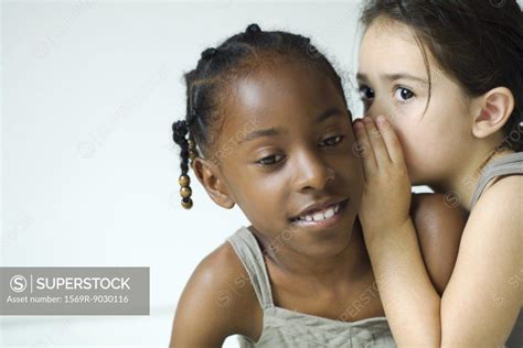 Girl Whispering In Friend S Ear Close Up Superstock