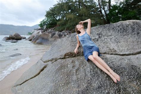 Young Caucasian Woman Lying On Stones On Sea Shore In Morning Wearing Jeans Sundress Stock