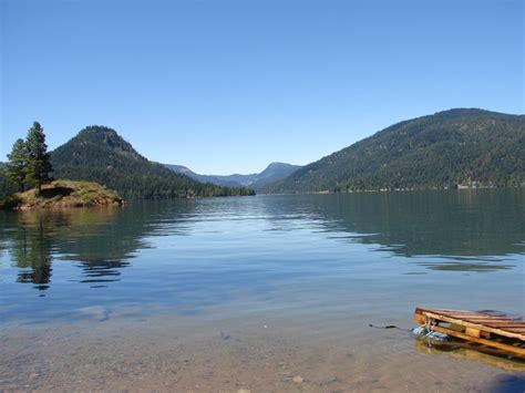 A Small Boat Sitting On Top Of A Lake Next To A Forest Covered Mountain