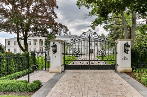 An Iron Gate In Front Of A White House With Trees And Bushes On Either Side