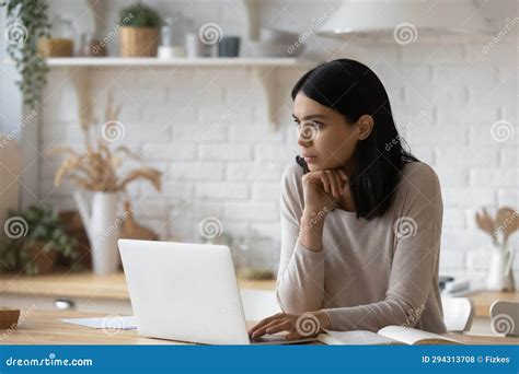 Thoughtful Asian Woman Sitting At Table With Laptop Pondering Stock