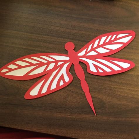 A Paper Cut Out Of A Dragonfly Sitting On Top Of A Wooden Table