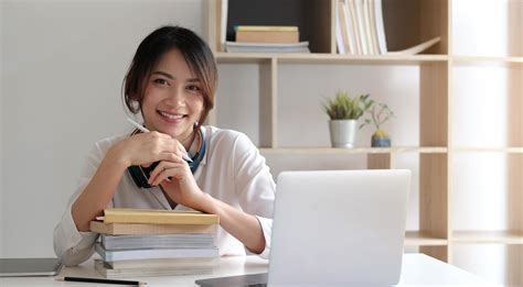 Smiling Asian Woman Working On The Desk With Books And Laptop Computer