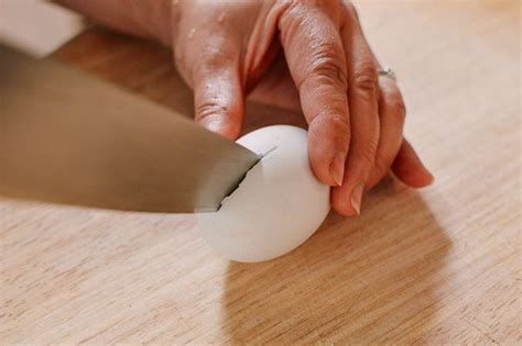 An Older Woman Is Peeling An Egg With A Knife On A Wooden Surface Close Up