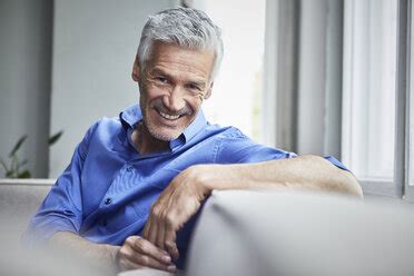 Portrait Of Laughing Mature Man Sitting On Couch At Home Stock Photo